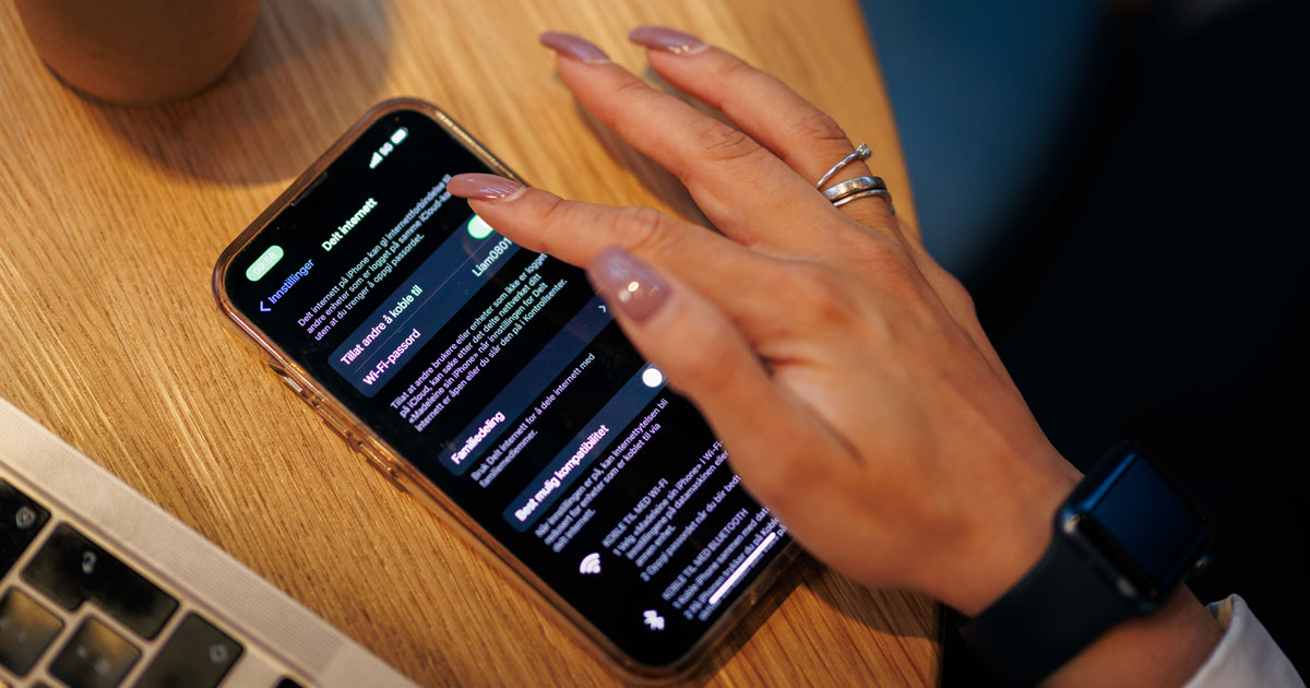 Mobil hvor vi ser meny for nettverksinnstillinger ligger på et bord, kvinnehånd rører mobilen.